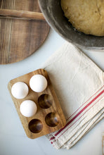 Load image into Gallery viewer, Wooden egg holder with eggs on a white surface next to a towel and rolling pin.